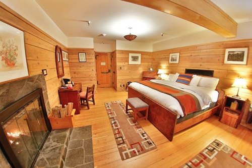 Cozy hotel room with wooden walls, a king bed, fireplace, and rustic decor, featuring a warm and inviting atmosphere.