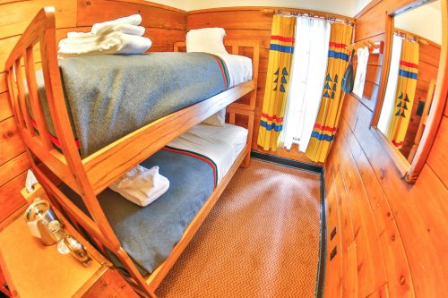 Cozy wooden room with bunk beds, colorful curtains, and a mirror, featuring a warm, rustic design.
