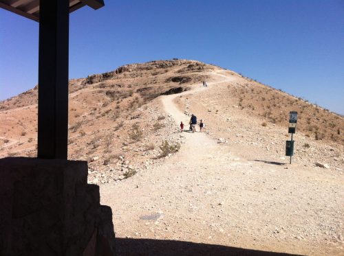A dirt path leads up a hill, with a few people walking towards the top under a clear blue sky.