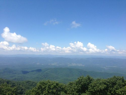 A panoramic view of lush green mountains under a bright blue sky with fluffy white clouds.