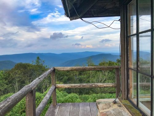 View from a rustic cabin balcony overlooking rolling mountains and a blue sky with scattered clouds.