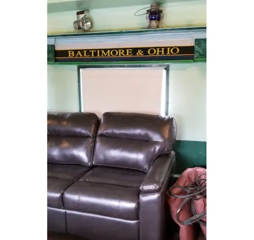 A leather couch in a room with a "Baltimore & Ohio" sign above a window covered by a blind.