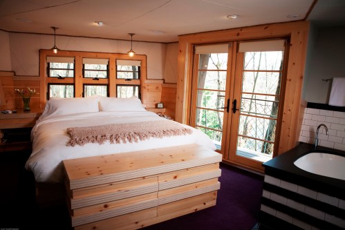 Cozy bedroom with a large bed, wooden accents, and sliding glass doors leading to a balcony with forest views.