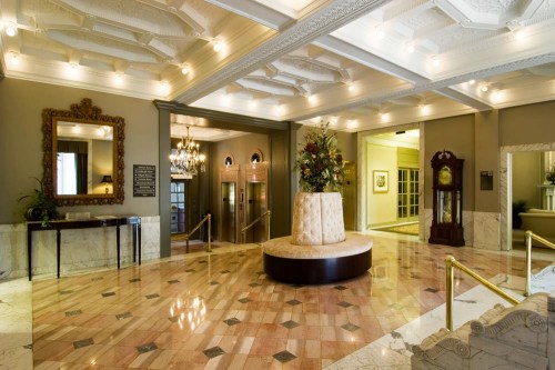 Elegant hotel lobby featuring marble floors, ornate ceiling, floral arrangement, and vintage clock.