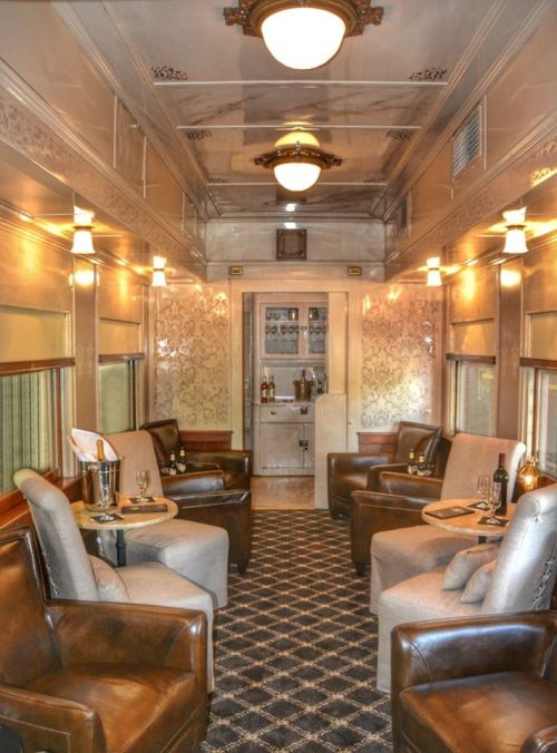 Luxurious train car interior featuring plush seating, elegant decor, and a bar area with soft lighting.
