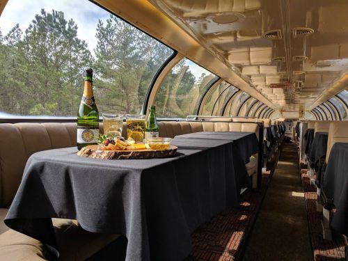 Interior of a train dining car with tables set for a meal, featuring drinks and a charcuterie board.