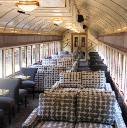 Interior of a vintage train car featuring plush seating and large windows, creating a cozy, elegant atmosphere.
