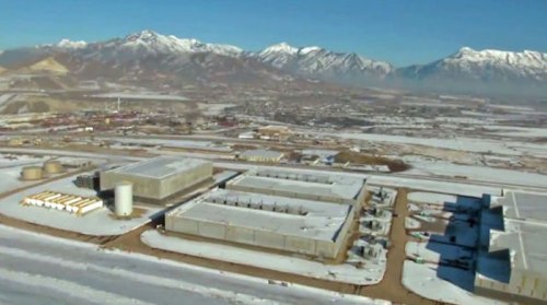 Aerial view of a snowy landscape with industrial buildings and mountains in the background.