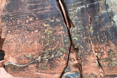 Ancient petroglyphs etched into a rocky surface, depicting various symbols and figures in earthy tones.