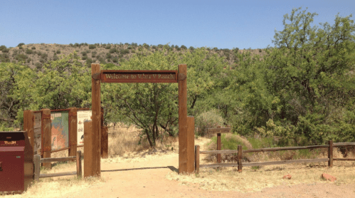 Wooden entrance sign reading "Welcome to V Bar V Ranch" surrounded by trees and a clear blue sky.