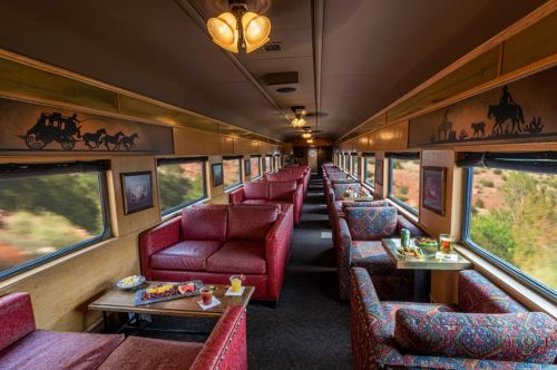 Interior of a vintage train car featuring red upholstered seating, tables, and large windows with scenic views.