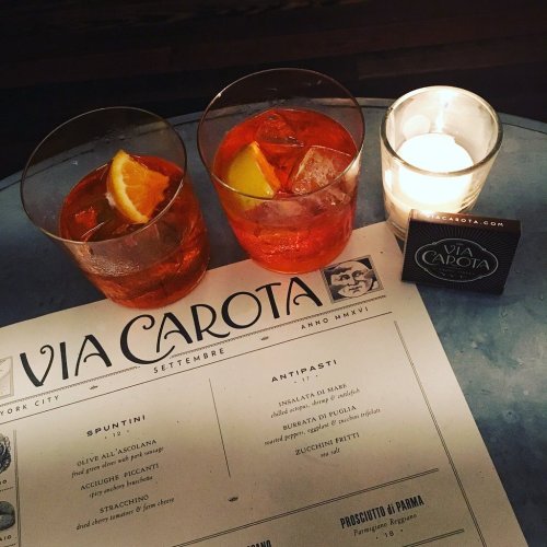 Two cocktails with citrus garnishes on a table with a menu and a lit candle, creating a cozy dining atmosphere.