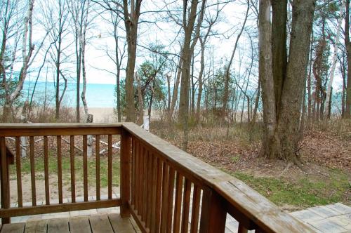 View from a wooden deck overlooking a sandy beach and lake, surrounded by bare trees and a cloudy sky.
