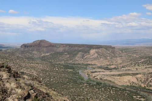 A panoramic view of a plateau surrounded by rolling hills and a winding river under a blue sky with scattered clouds.