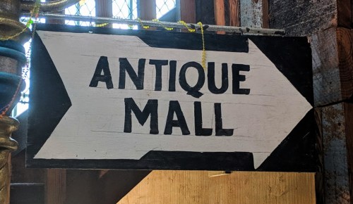 Sign pointing left with the text "ANTIQUE MALL" in bold black letters on a white background.