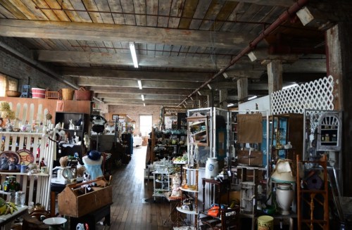 A spacious antique shop filled with various vintage items and furniture, featuring wooden beams and rustic decor.