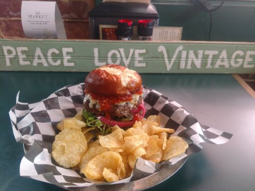 A delicious burger on a plate with chips, set against a backdrop of a vintage sign reading "Peace Love Vintage."