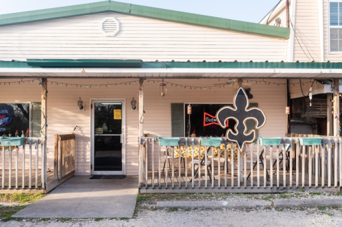 A quaint restaurant exterior with a green roof, wooden railing, and a large fleur-de-lis symbol on the wall.