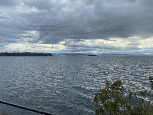 A serene lake view under a cloudy sky, with distant mountains and a small island visible on the horizon.