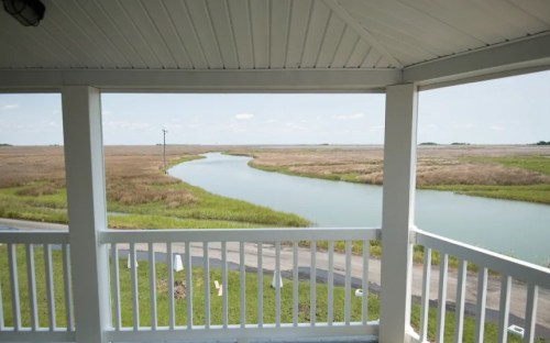 View from a porch overlooking a winding river and marshland under a clear blue sky.