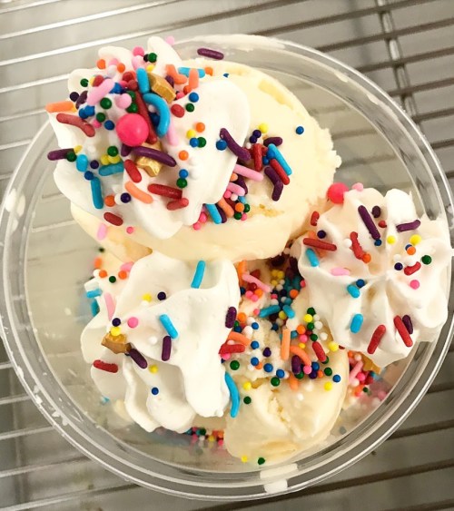 A clear cup filled with scoops of ice cream topped with whipped cream and colorful sprinkles.