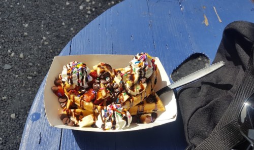 A dessert bowl with waffles topped with whipped cream, chocolate chips, strawberries, and colorful sprinkles on a blue table.