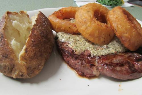 A plate featuring a juicy steak topped with seasoning, crispy onion rings, and a baked potato.