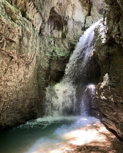 A serene waterfall cascading down rocky cliffs into a tranquil pool below, surrounded by lush greenery.