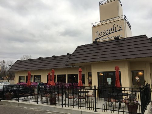 Exterior of Joseph's Restaurant & Bar, featuring a patio with red umbrellas and flower beds under a cloudy sky.