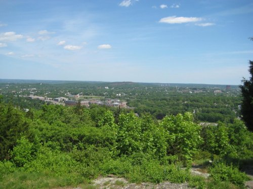 A panoramic view of a lush green landscape under a clear blue sky, with distant hills and a small town visible.