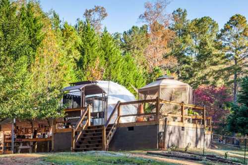 Two glamping tents on a wooden deck surrounded by trees, with a cozy outdoor seating area below.