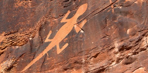 Petroglyph of a lizard etched into a rocky surface, showcasing ancient rock art against a textured brown background.