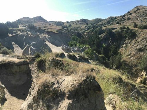 A scenic view of rolling hills and rocky terrain, with greenery in the valley below under a clear blue sky.