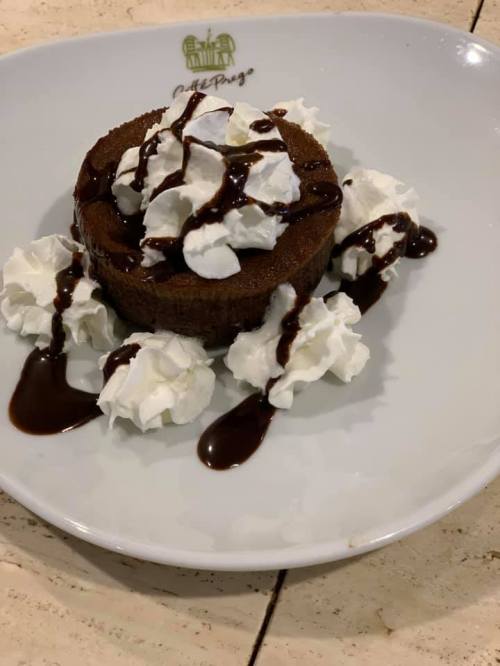 A round chocolate dessert topped with whipped cream and chocolate sauce, served on a white plate.