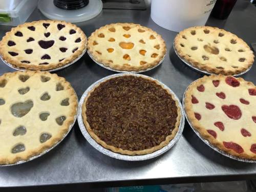 A variety of six pies on a table, featuring different fillings and heart-shaped cutouts in the crusts.
