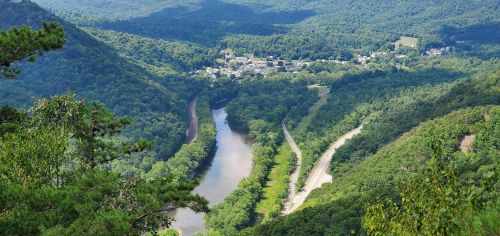 Aerial view of a winding river surrounded by lush green mountains and a small town nestled in the valley.