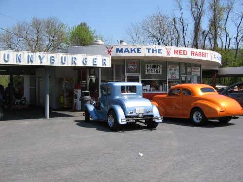 A vintage diner named "Sunnyburger" with classic cars parked outside, surrounded by trees and a clear sky.