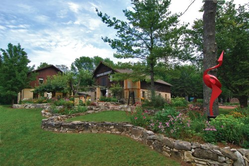 A scenic view of a building surrounded by lush greenery, flowers, and a red sculpture in a landscaped garden.
