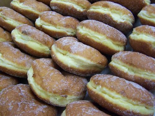 A close-up of freshly made donuts dusted with sugar, filled with cream, arranged in a neat pile.