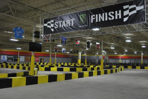 Indoor go-kart track featuring a "START" and "FINISH" banner, with yellow and black barriers and racing jerseys displayed.