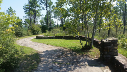 A winding stone path leads through a green landscape with trees and a stone wall on the right.