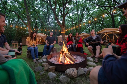 A group of friends gathered around a campfire, enjoying music and conversation in a cozy outdoor setting.