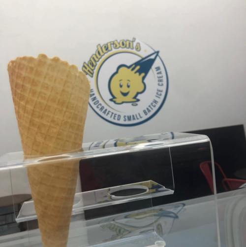 A waffle cone in front of a sign for Henderson's handcrafted small batch ice cream.