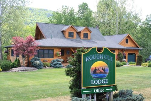 A rustic lodge with a wooden exterior, surrounded by greenery, featuring a sign that reads "Rough Cut Lodge."