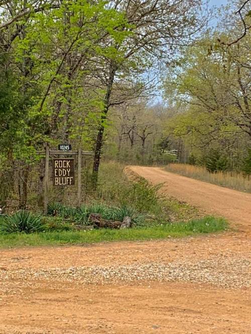 A dirt road leads to a sign reading "Rock Eddy Bluff," surrounded by trees and greenery.