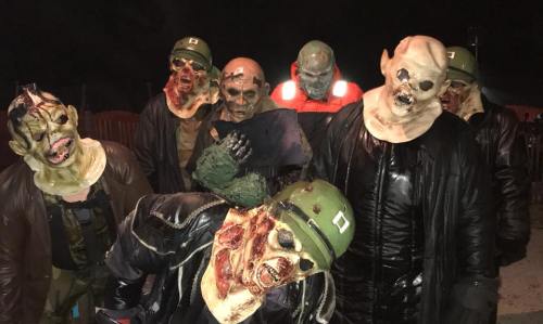A group of people in creepy zombie costumes, wearing military helmets and grotesque masks, posing in a dark setting.