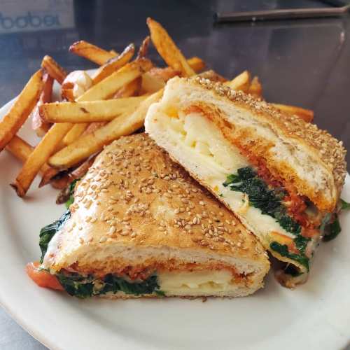 A sesame seed sandwich filled with spinach, cheese, and sauce, served with a side of golden French fries.