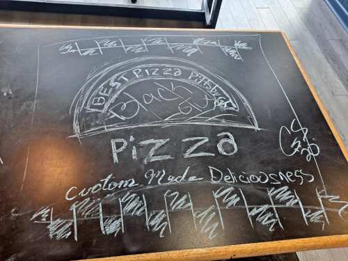 Chalkboard drawing advertising "Best Pizza Pittsburgh" with the words "Custom Made Deliciousness" and decorative borders.
