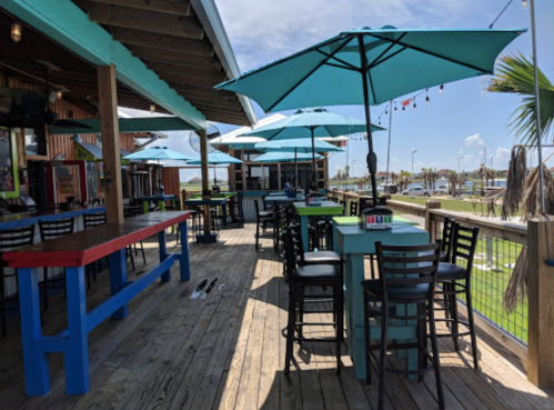 Outdoor dining area with colorful tables and umbrellas, overlooking a sunny waterfront.