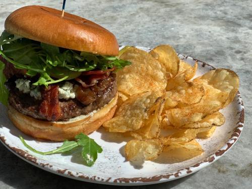 A juicy burger with bacon, lettuce, and blue cheese, served with a side of crispy potato chips on a plate.